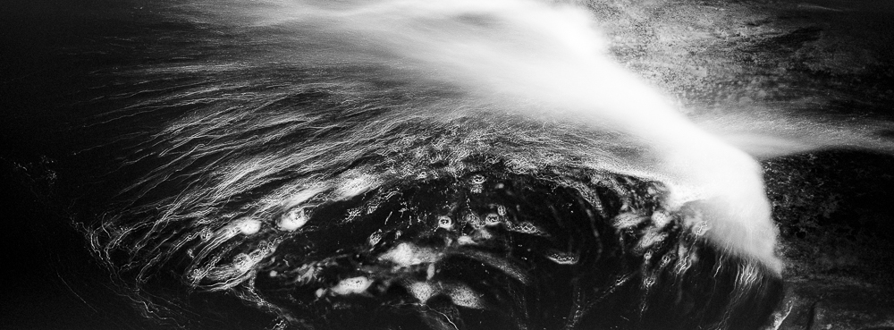 A monochrome image of swirling foam in a river at night.